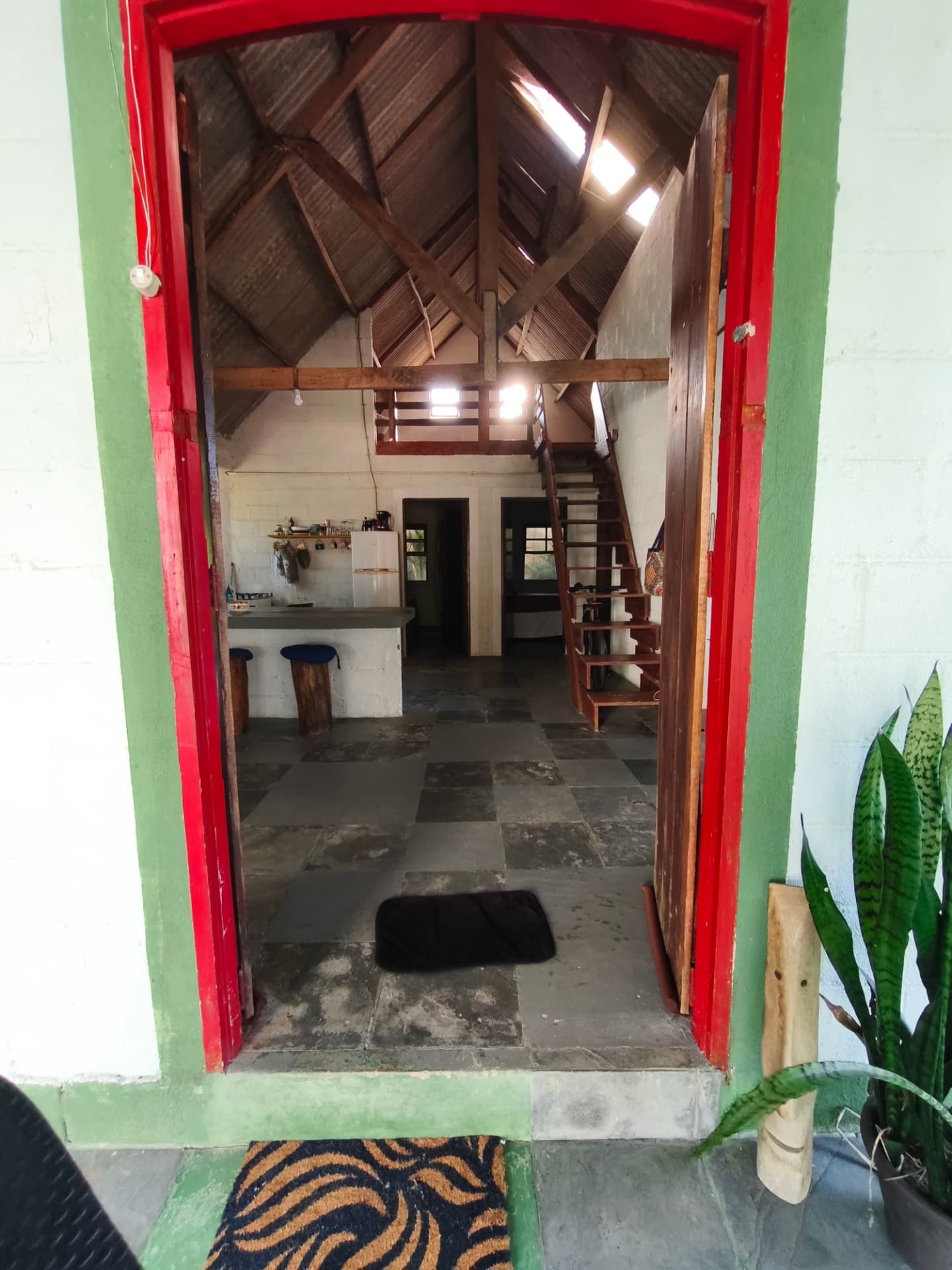Entrada da casa pela porta vermelha, com pé-direito alto de madeira