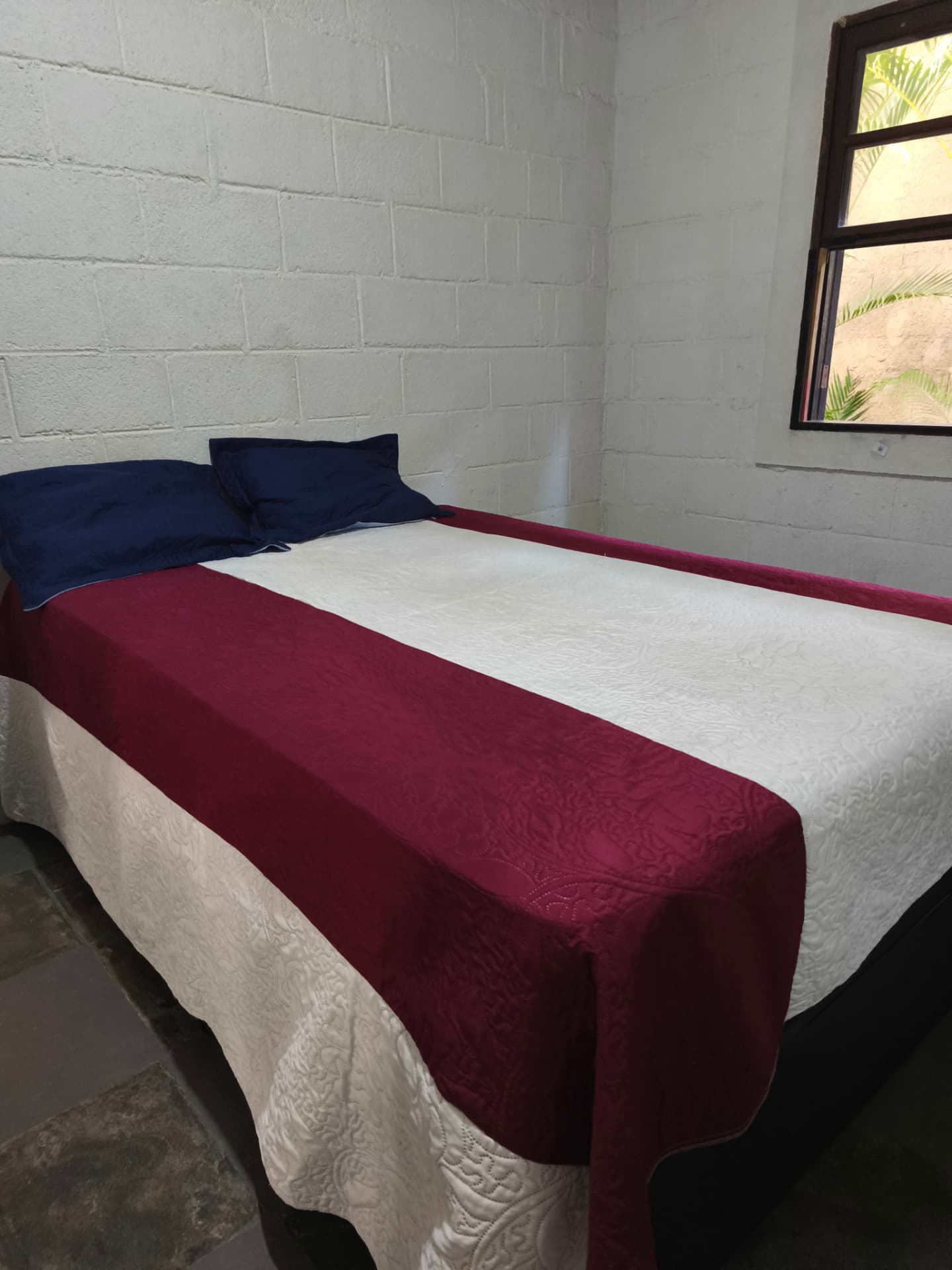 Quarto com colcha bordô e janela para o verde