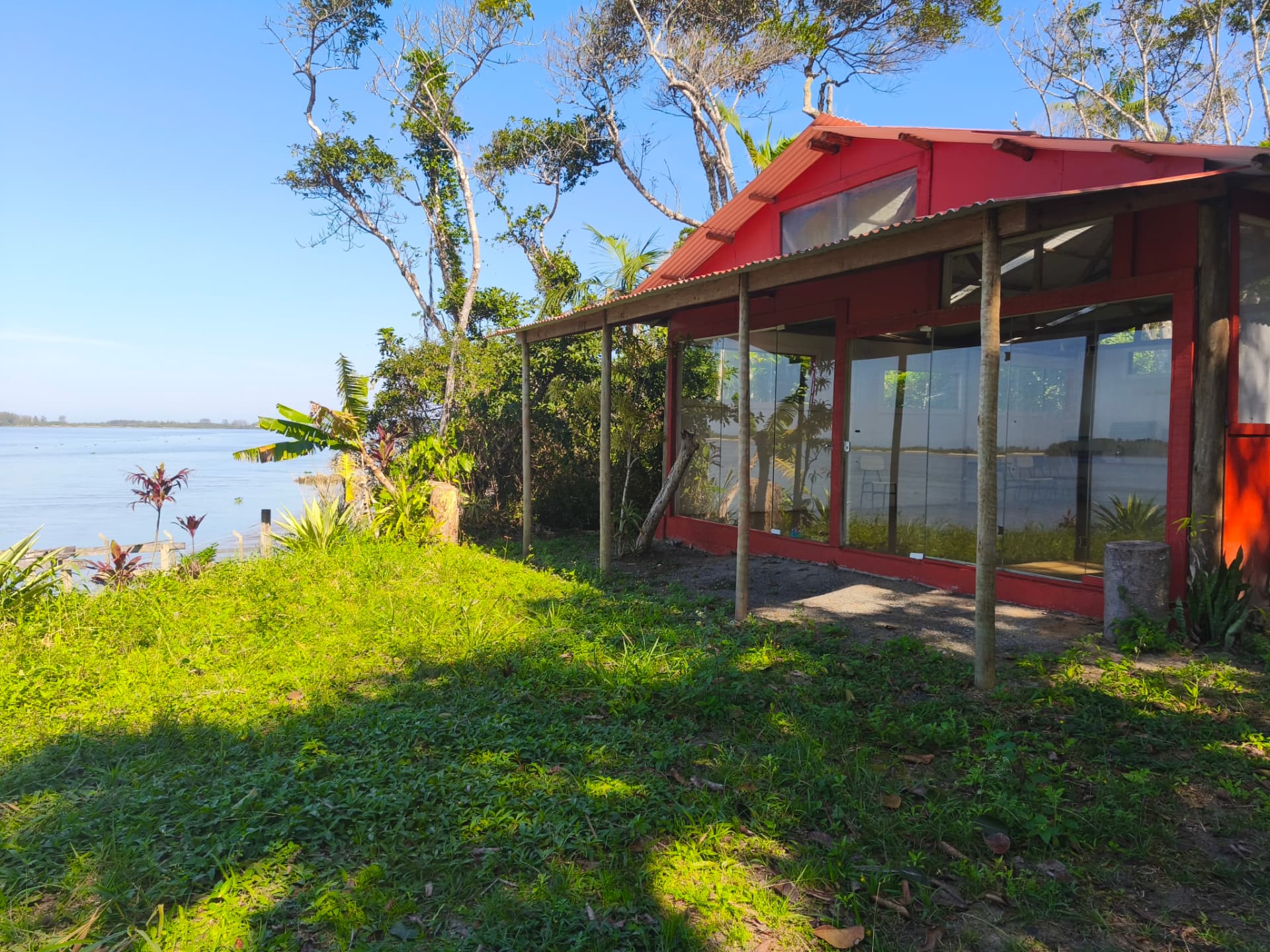 Salão de vidro vermelho à beira do rio, cercado de mata